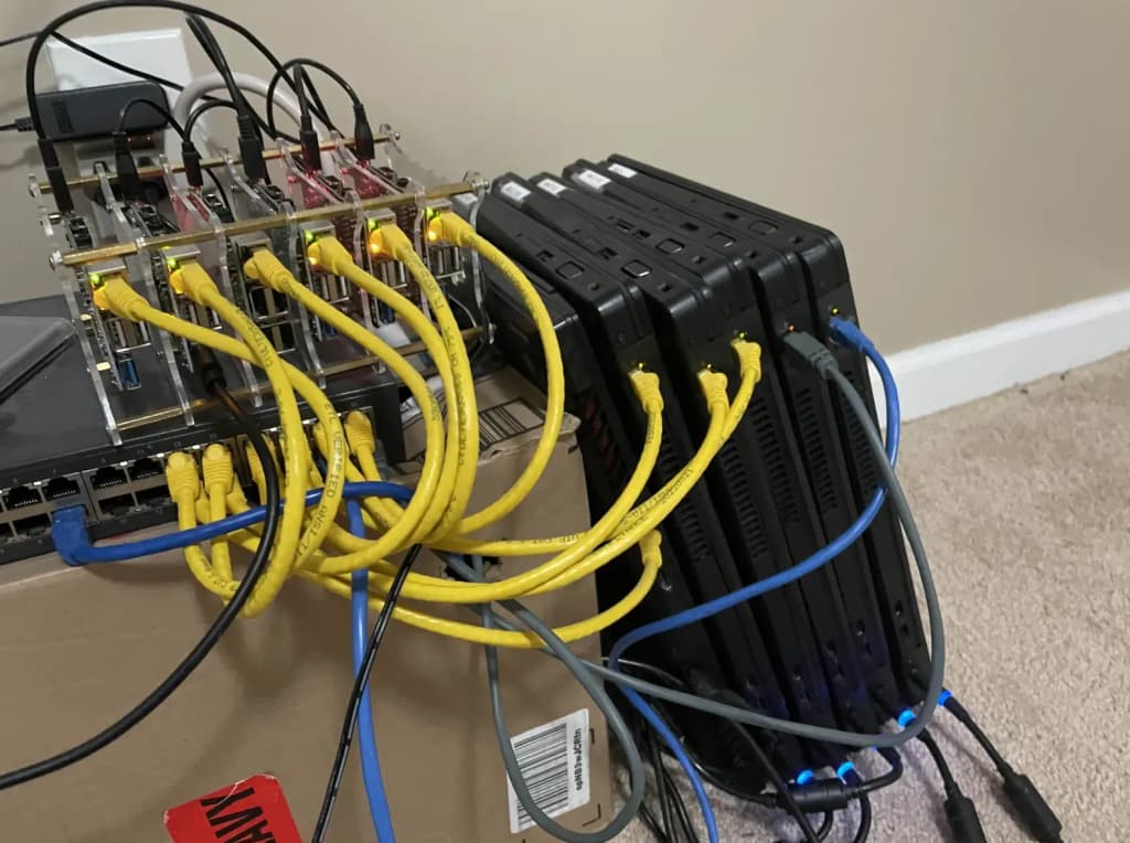 A toddler crouched next to a pile of laptops, Raspberry Pis, and single-board computers forming a home Kubernetes cluster